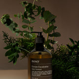 Bottle of mosey Eucalyptus Body Cleanser / Body Wash with plants & leaves representing the fragrance. Such as eucalyptus, Cedarwood & Neroli Blossom